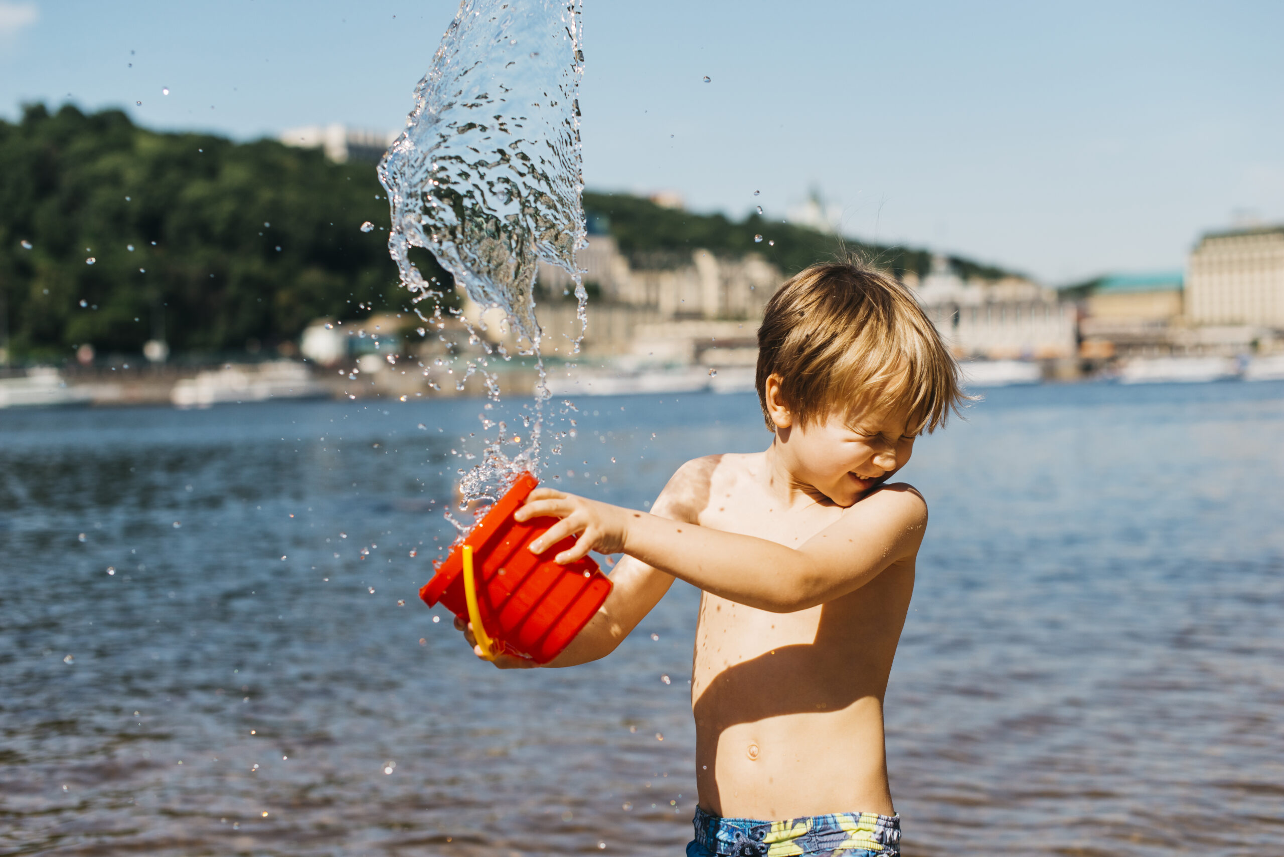 Niño jugando con un cubo de agua en la playa.